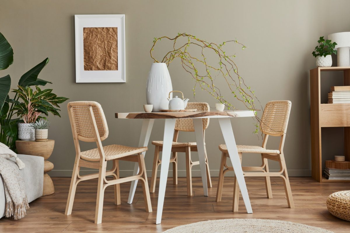 Aménagement intérieur d'une salle à manger élégante avec table familiale en bois et époxy, chaises en rotin, fleurs dans un vase et théière avec tasses.